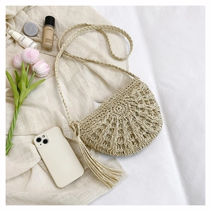 Detail of straw woven crossbody bag with hollow design and tassel on soft fabric
