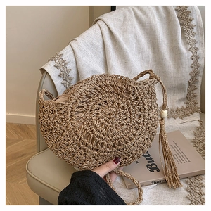 Detail of round straw shoulder bag featuring woven texture and tassel on a chair