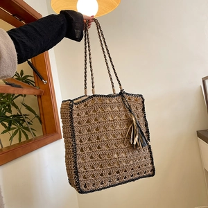 Handwoven straw tote bag with black trim and tassel detail, shown held in hand