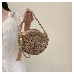 Detail of round straw bag with natural woven texture, stylish tassel, and bead accent