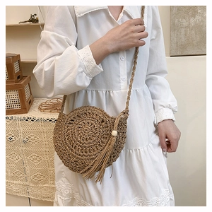 Detail of round straw woven crossbody bag featuring decorative tassels and wooden bead