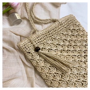 Detail of beige crochet woven bag with fringe tassel and wooden beads on linen