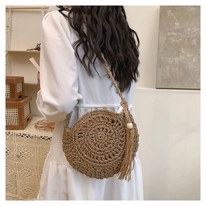 Detailed close-up of a handmade straw shoulder bag featuring a unique spiral weave and tassel