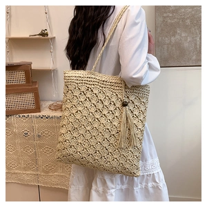 Detail of hand-woven straw shoulder bag featuring decorative wooden beads and fringe tassels
