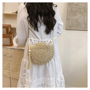Detail of hand-woven beige straw crossbody bag with decorative fringe and wooden bead