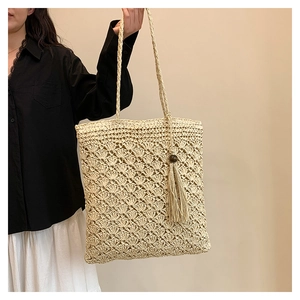 Detail of beige hand-woven tote bag showing crochet patterns and tassel with wooden beads