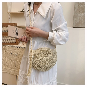 Close-up of handmade woven round straw bag with decorative fringe and long shoulder strap