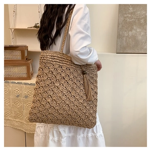 Detail view of woven straw tote bag with crochet texture and long fringe tassel decoration