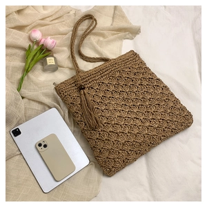 Detail of woven straw tote bag with zip closure and tassel on a beige fabric background