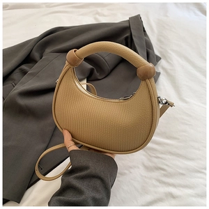 Detail of a beige half-moon handbag featuring thick handles and decorative round spheres