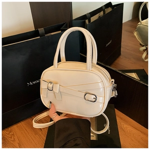 Detail of cream glossy mini handbag showing crisscross straps and silver buckle finish