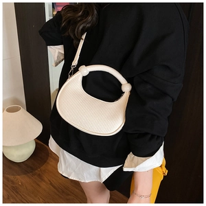 Detail of cream-white crescent bag featuring vertical pleated texture and silver hardware