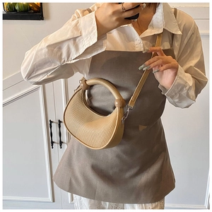 Detail of beige pleated half-moon bag featuring vertical textures and round metal handle