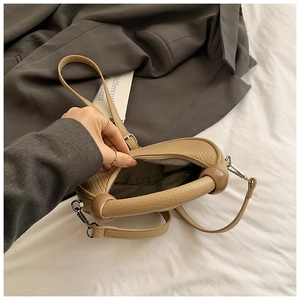 Detail of khaki leather handbag featuring dark resin rings and smooth zipper closure