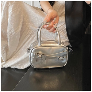Detailed close-up of metallic silver handbag featuring bow accent and zipper closure