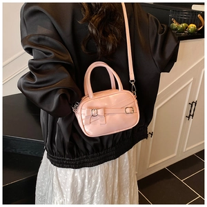 Pink patent leather mini crossbody bag with bow detail worn by a model in a casual setting