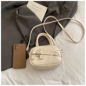 Detail of cream white PU leather crossbody bag with decorative bow and metal buckle accent