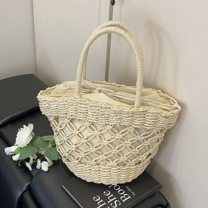 Straw tote bag with hollow grid weave and drawstring liner on black surface