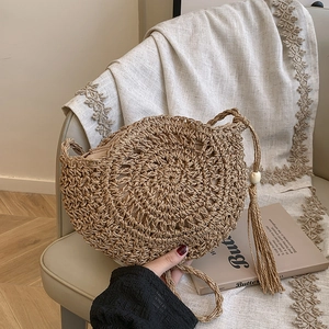 Handwoven round straw crossbody bag with long tassel and fabric lining on linen chair