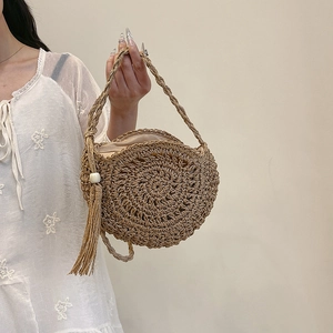 Handwoven straw shoulder bag with long tassel and bead detail held by woman in lace dress