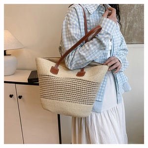 Detail of striped woven straw tote bag featuring brown leather handles for summer vacations
