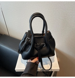Close-up of black lychee grain leather handbag with hammock style and metal buckles