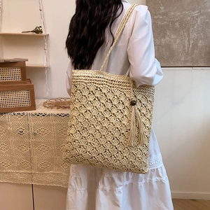 Beige handwoven straw tote bag with tassel charm and bohemian hollow pattern for women