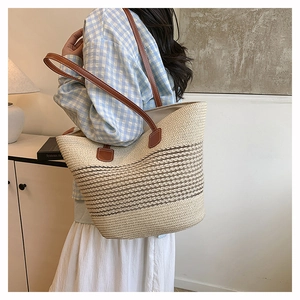 Detail of large straw tote bag with brown leather shoulder straps and striped texture
