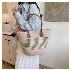 Detail of striped woven straw tote with brown leather handles and reinforced buckle