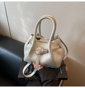 Close-up of silver lychee grain handbag featuring buckle strap detail on a book