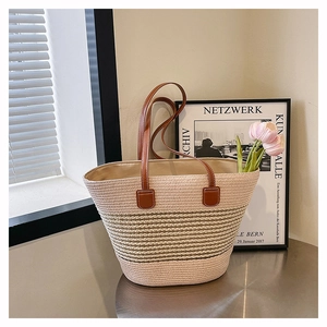 Detail of a striped straw tote bag with brown leather handles and premium stitching