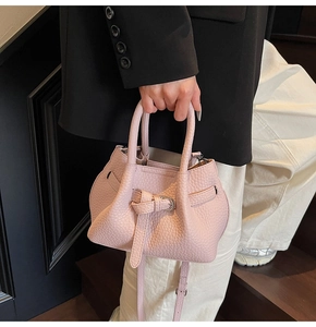 Close-up of pink lychee grain leather handbag with elegant draped texture and handles