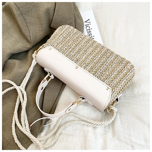 Detail of woven straw handbag featuring white leather flap, gold studs, and rope strap