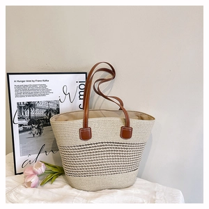 Detail of straw tote bag with brown stripes and leather handles in a summer setting