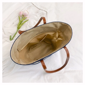 Interior view of large straw tote bag with beige lining, zipper pocket, and leather straps