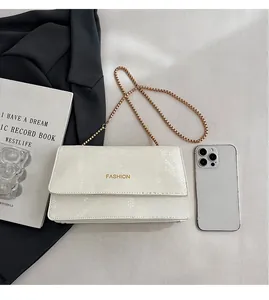 Close-up of white snake-embossed chain bag with gold Fashion lettering and metal strap