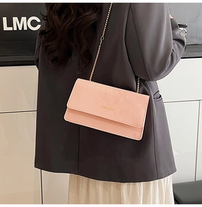 Chic pink lizard-embossed crossbody bag with gold chain strap worn by a stylish model