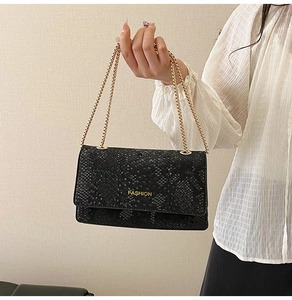 Detail of black faux snakeskin texture on handbag with gold FASHION metal lettering