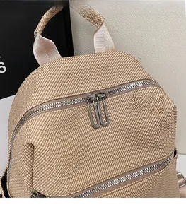 Detail of khaki woven backpack showing dual silver metal zippers and textured fabric