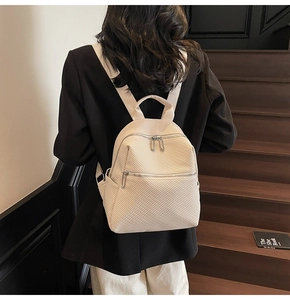 Detail of cream backpack with twill texture and silver zippers on a model's back