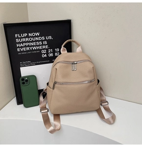 Detail view of beige woven texture backpack with front zippers on a minimalist display