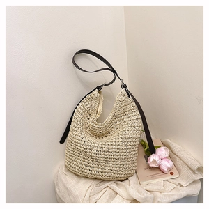 Detail of hand-woven straw shoulder bag with dark brown leather strap and metal ring buckle