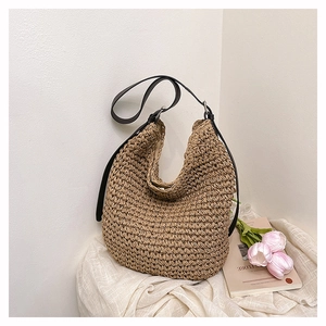 Close-up of woven straw hobo bag with black leather strap and metallic hardware