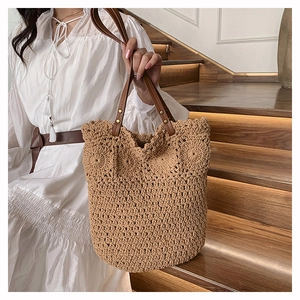 Detail of woven straw tote bag with brown leather handles and gold rivet accents