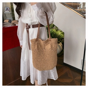Detailed close-up of a large beige woven tote bag with brown leather handles and rivets