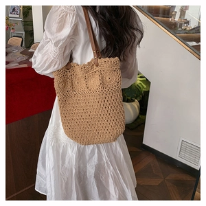 Detail of hand-woven straw tote with wavy edges and brown leather shoulder straps