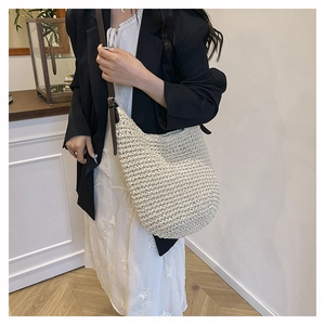 Detailed view of cream woven shoulder bag with brown leather strap worn by a model