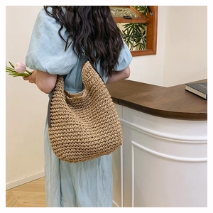 Detail of hand-woven straw tote bag with slim shoulder strap shown on a female model