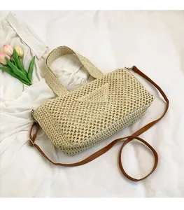 Detail of light beige woven straw bag with brown leather straps on white fabric