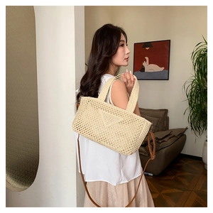 Detail of woven straw tote bag texture with brown leather strap and triangle patch
